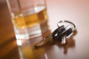 A set of car keys on a wooden table, set in front of a glass of whiskey.